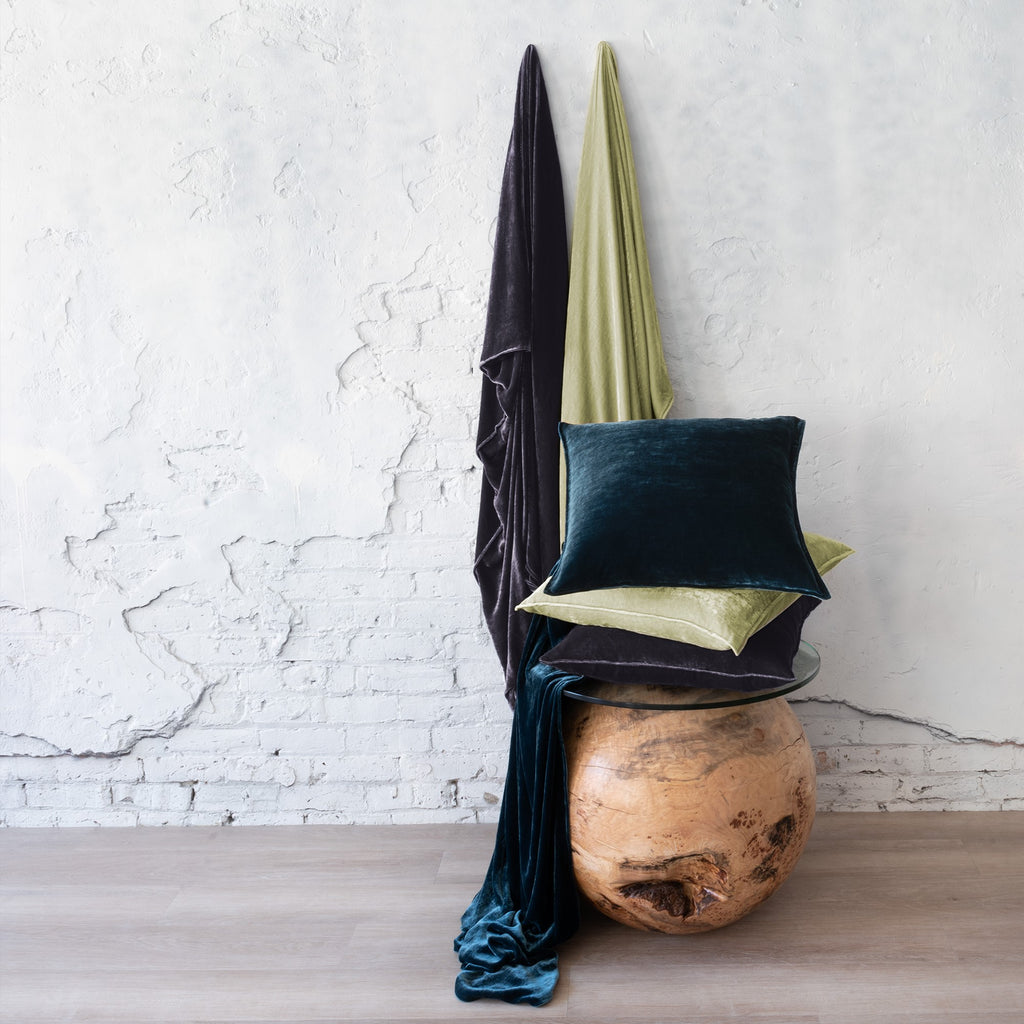 Divina Throws & Cushions - Hanging (left): Eclipse, (right): Celadon. Draped on table: Peacock. Cushions top-to-bottom: Peacock, Celadon and Eclipse